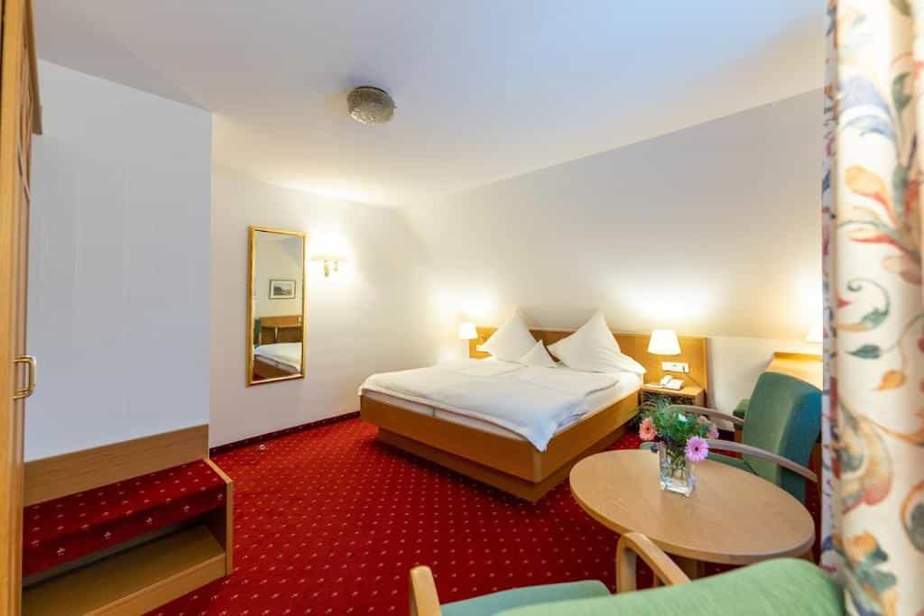 Hotel room with wooden bed, red carpet, and seating area, likely in Breisach.