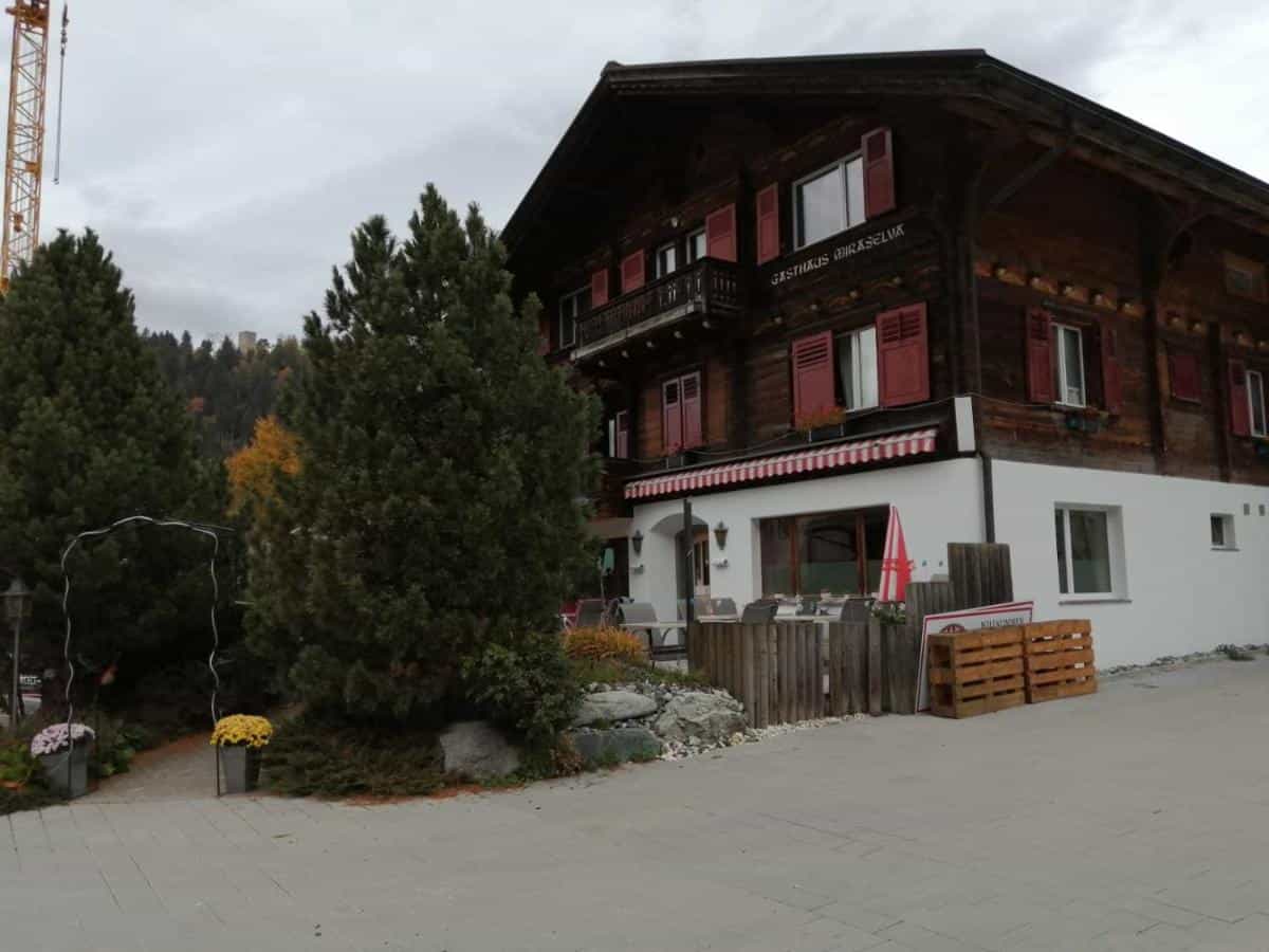 Gasthaus Miraselva wooden building with red shutters, outdoor seating, and trees.