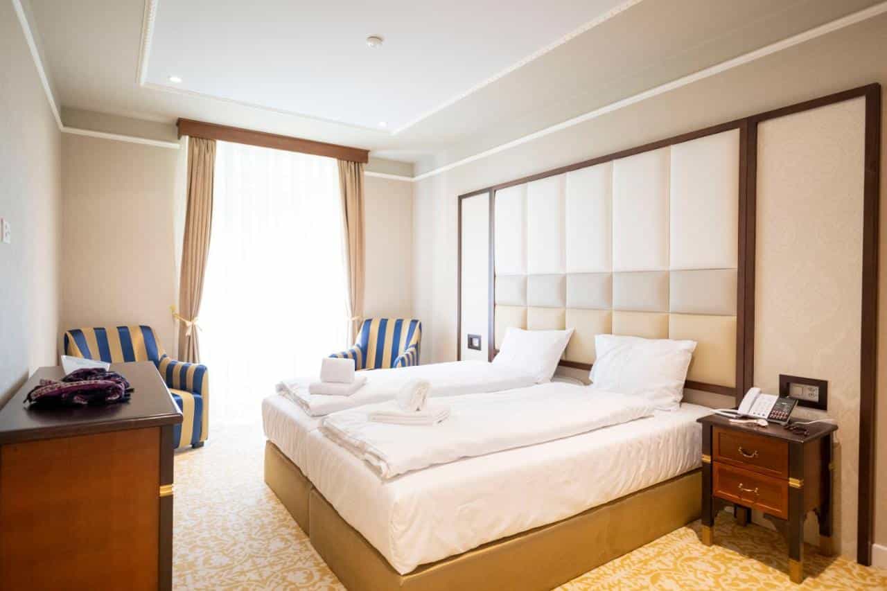 Twin beds with white linens in a hotel room at Scuol Palace with striped armchairs.