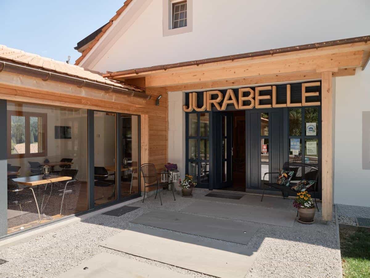 Entrance to Jurabelle building with wooden awning and outdoor seating in Yverdon-Les-Bains