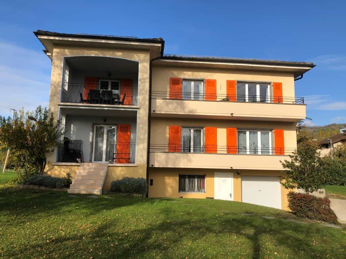 Yellow apartment building with orange shutters and green lawn in Lausanne, Au Bonheur des Iris.
