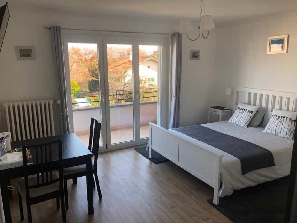 Bedroom with white furniture, dark wood table, and balcony view in Lausanne Au Bonheur des Iris.