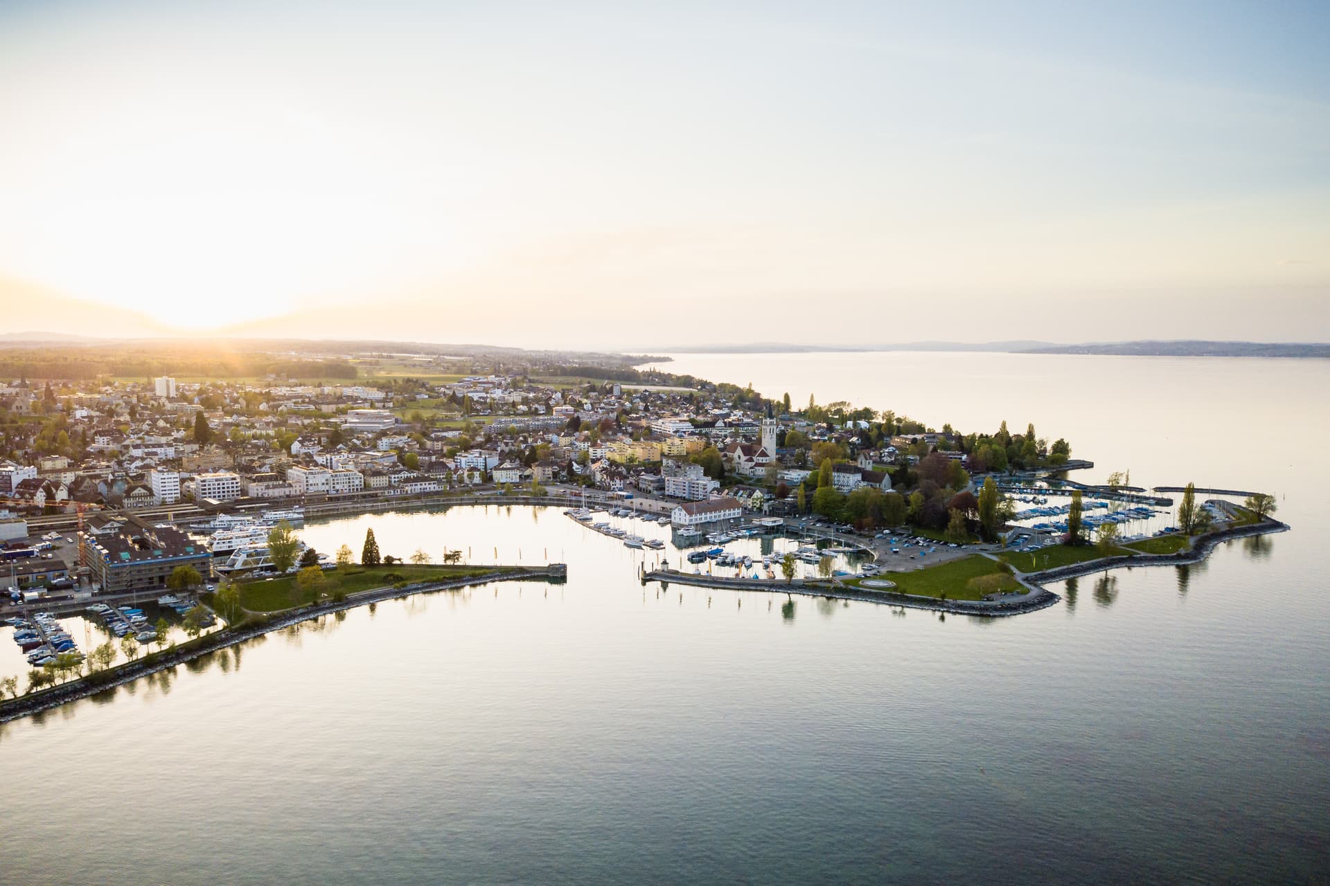 Ferry harbor with docked boats in Romanshorn, Switzerland, at sunset over the lake.