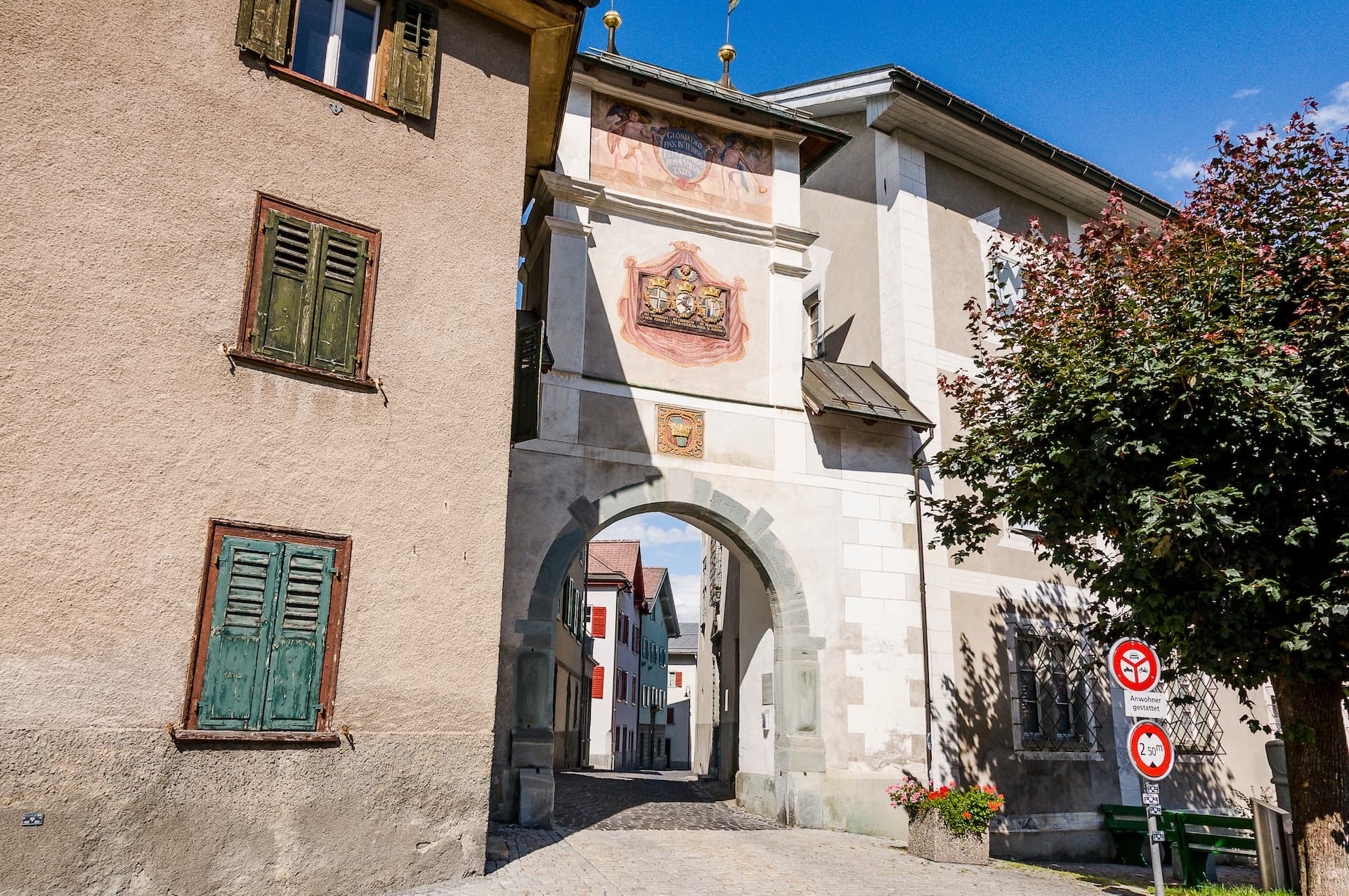 Arched stone gateway with painted facade in Ilanz, Switzerland leading to a narrow street.