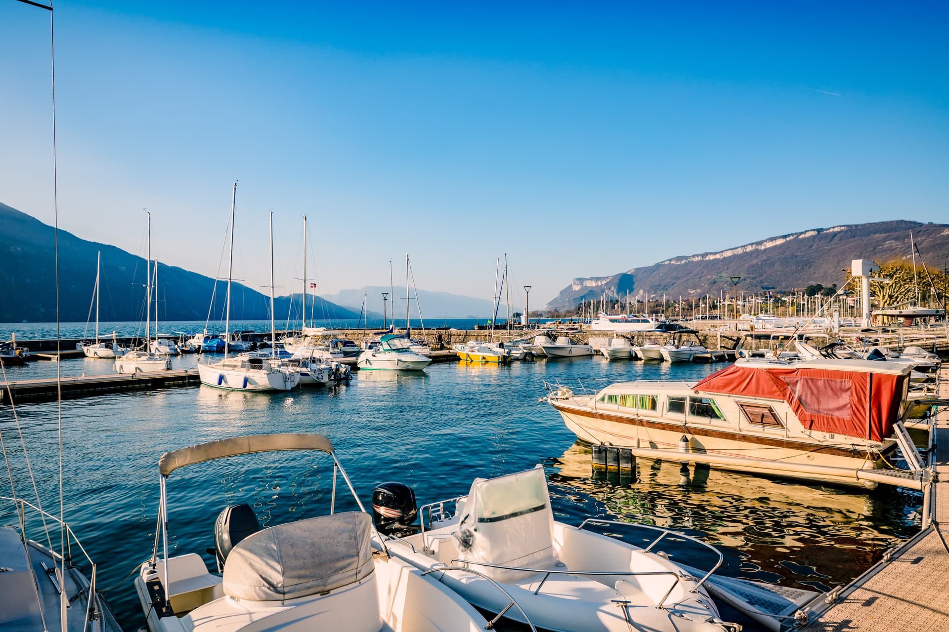 Boats docked in a marina on a lake with steep mountains in Aix-les-Bains.