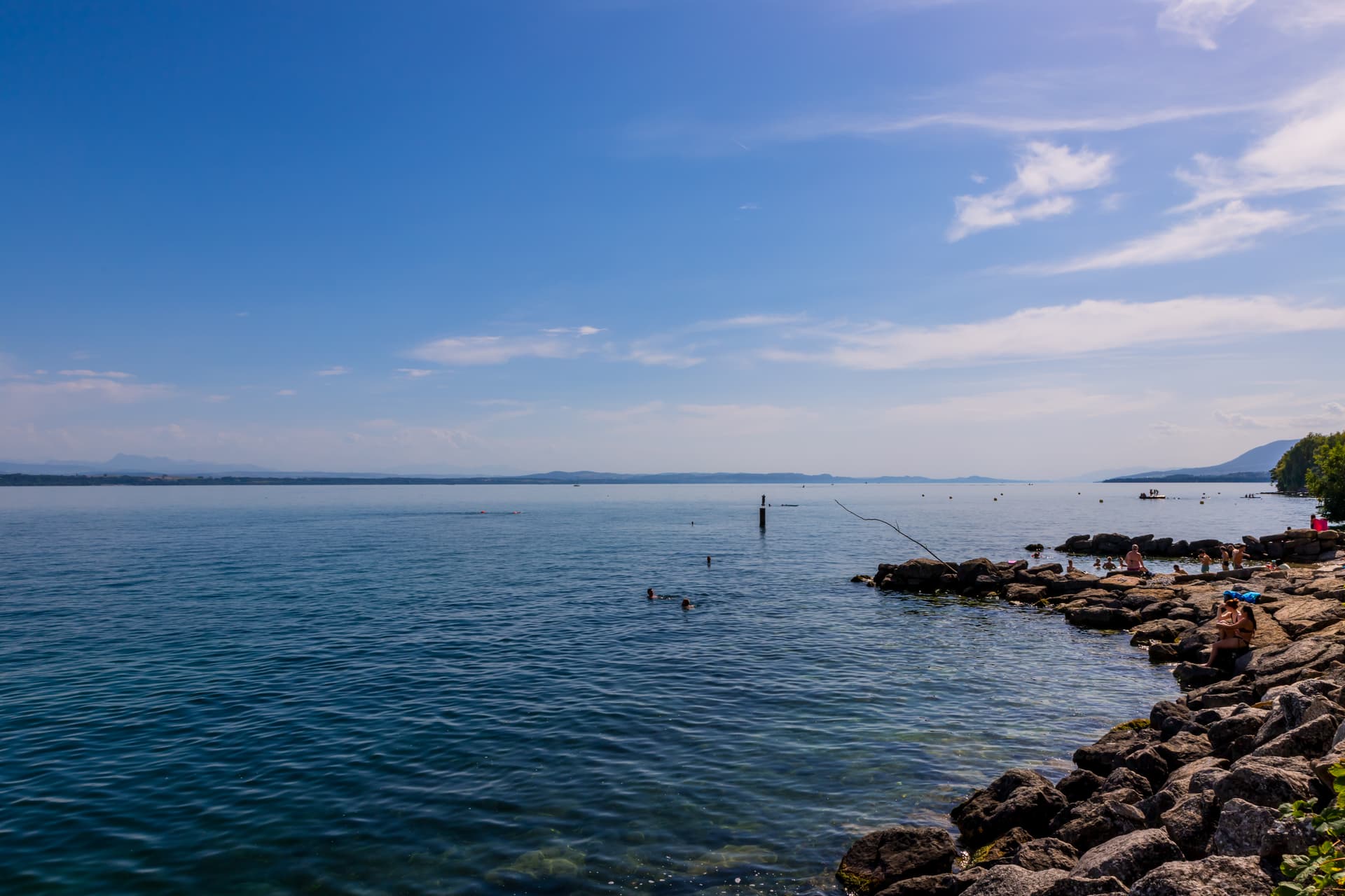 People swimming and sunbathing on rocky shore of Lake Neuchâtel, Switzerland.