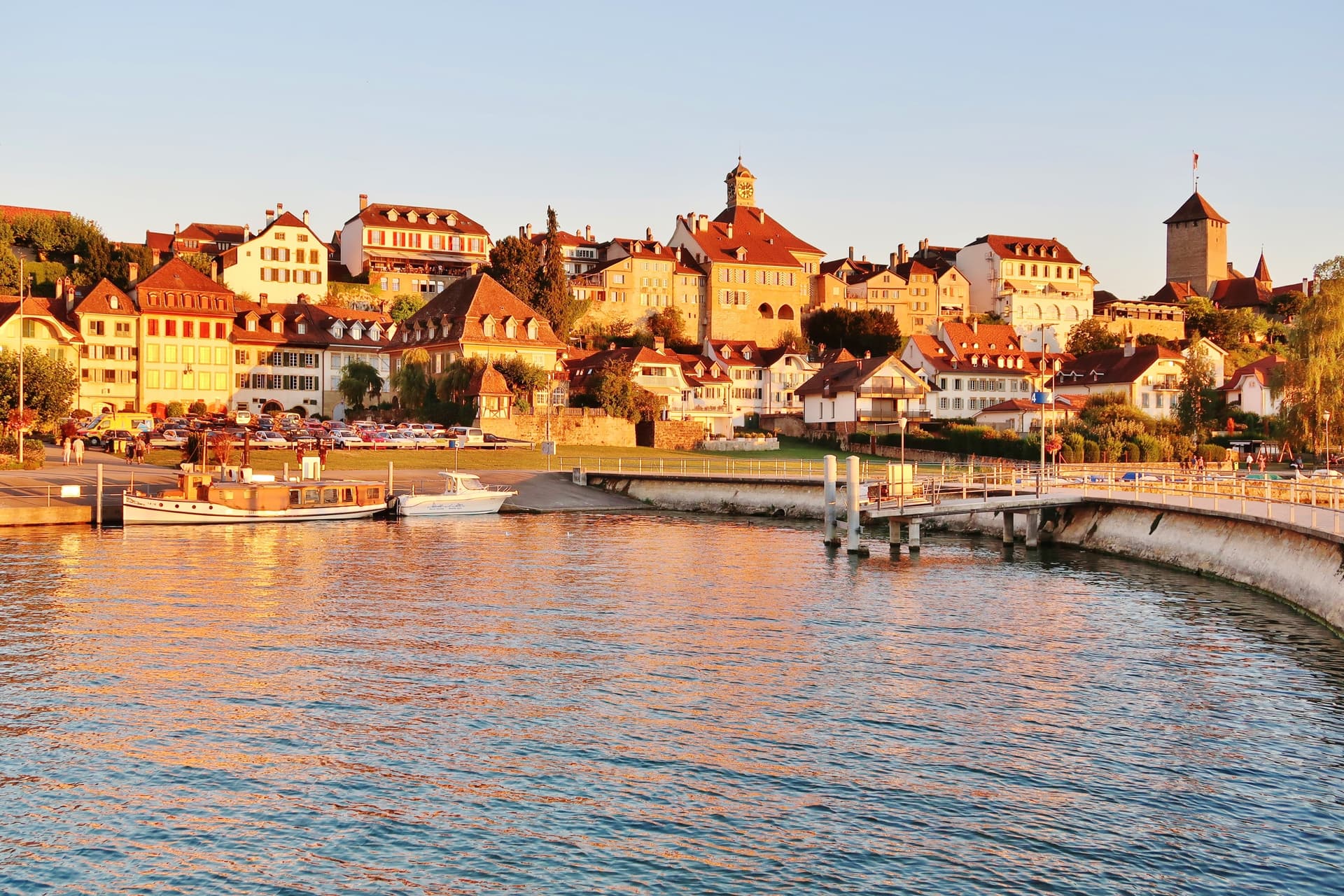 Murten, Westschweiz waterfront with historic buildings, boats, and water reflecting sunset light.