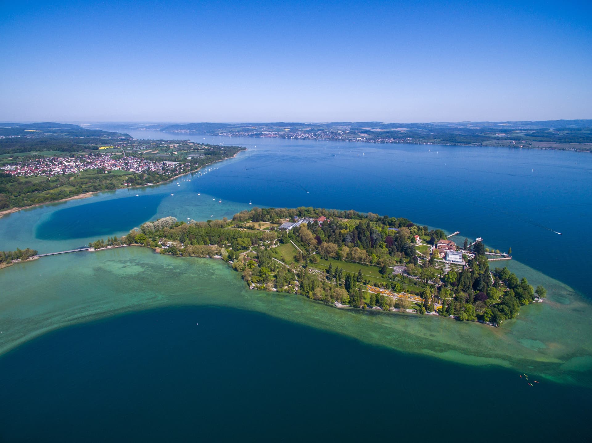 Aerial view of Insel Mainau with lush gardens and buildings surrounded by clear blue lake water.