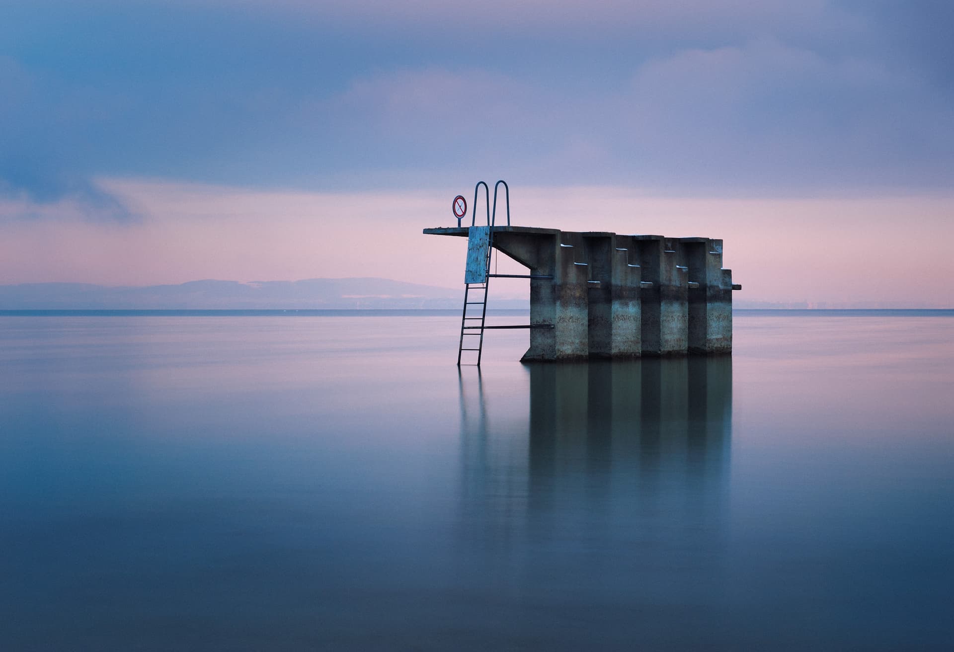 Diving platform structure in calm water at dusk with distant mountains, Arbon, Switzerland.
