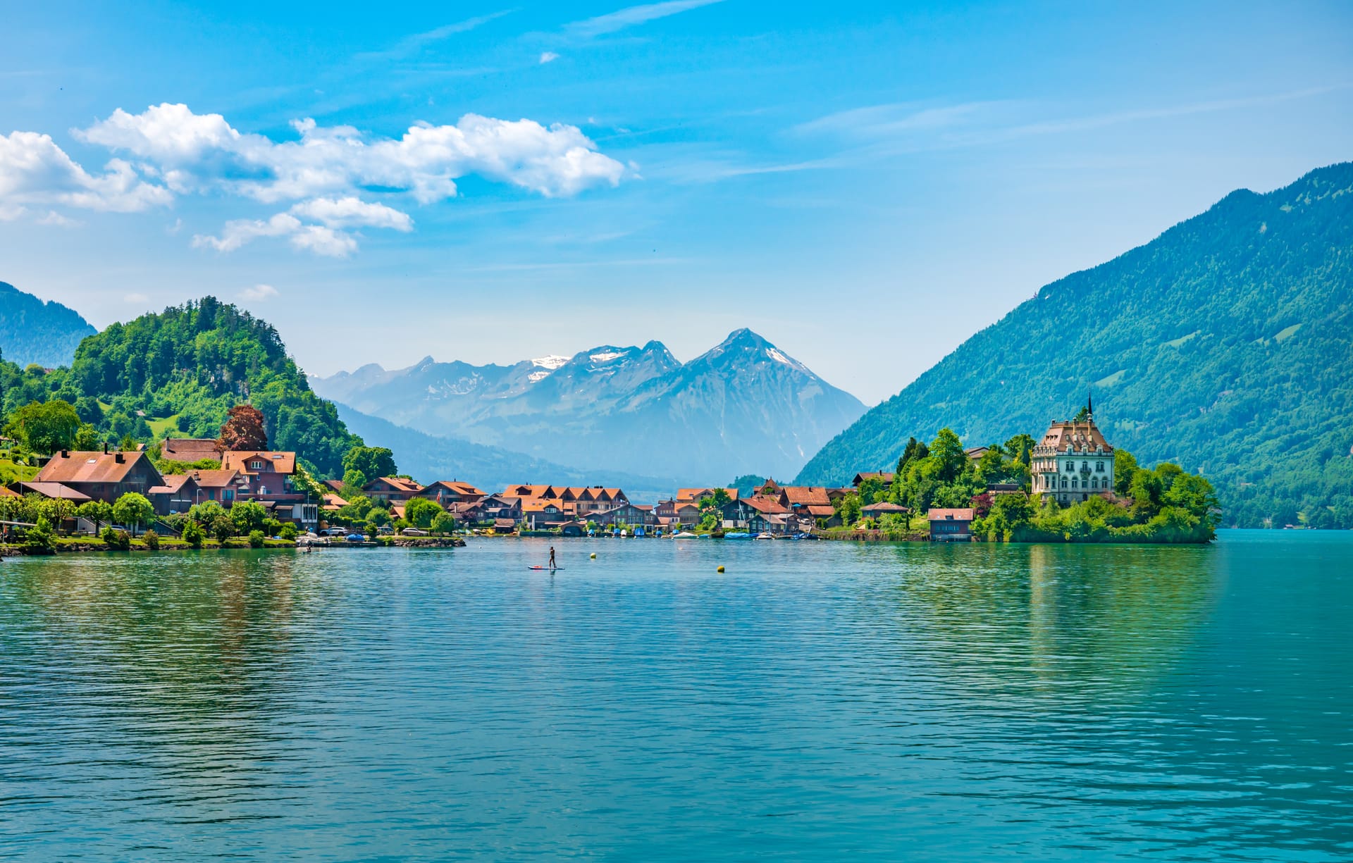 Stand-up paddleboarder on Lake Brienz with village and snow-capped Alps in background