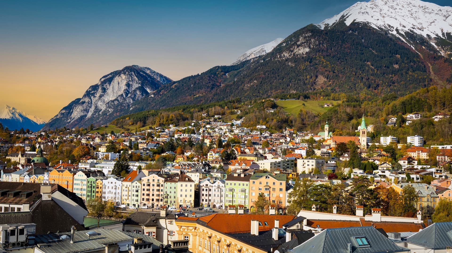 Panoramic view of Innsbruck cityscape with colorful buildings nestled against snow-capped Alpine mountains.