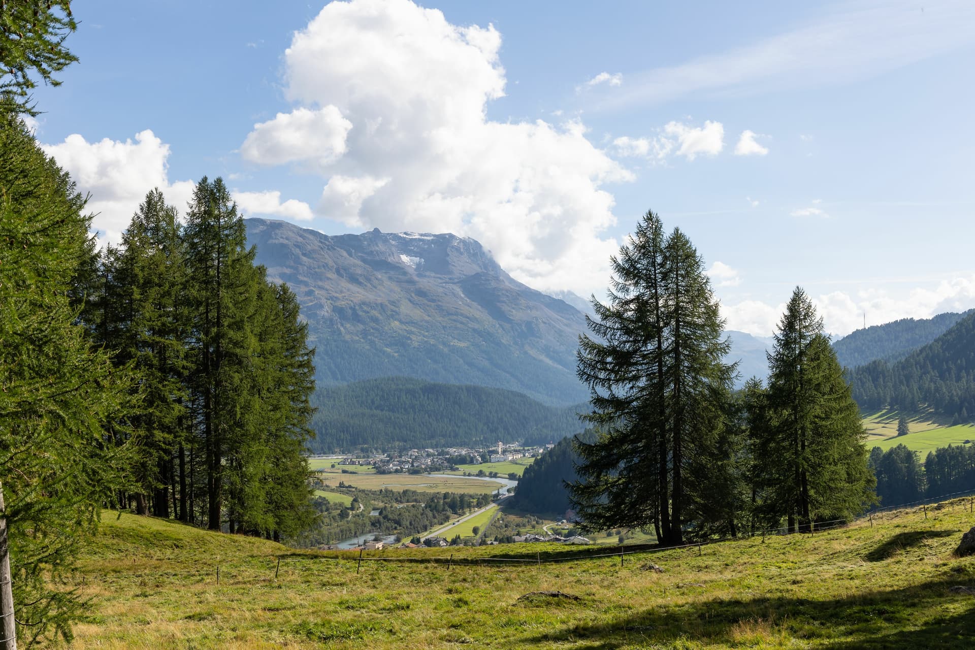 Scenic view of Samedan, Switzerland valley with village, river, and snow-capped alpine mountains.