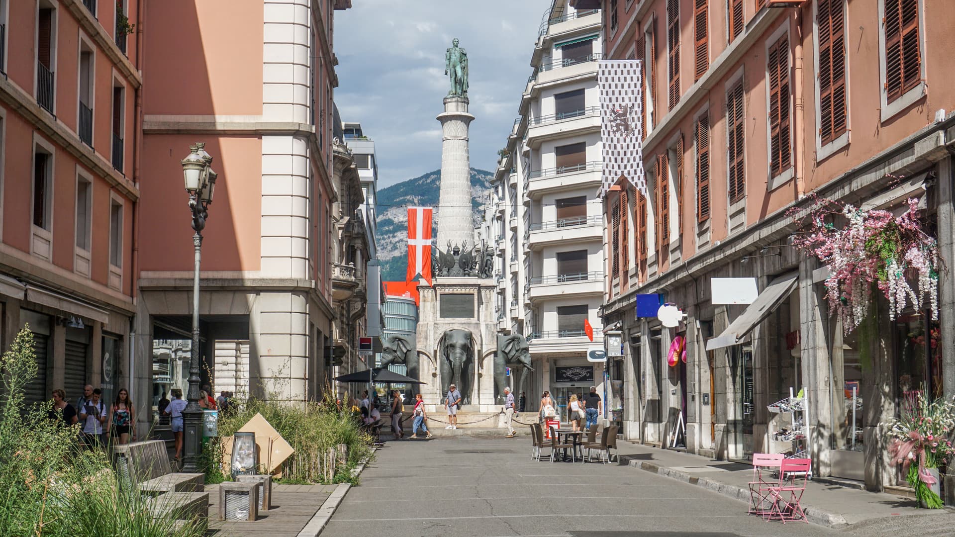 Statue on column at the Elephant Fountain in Chambéry, France, with buildings and mountains.