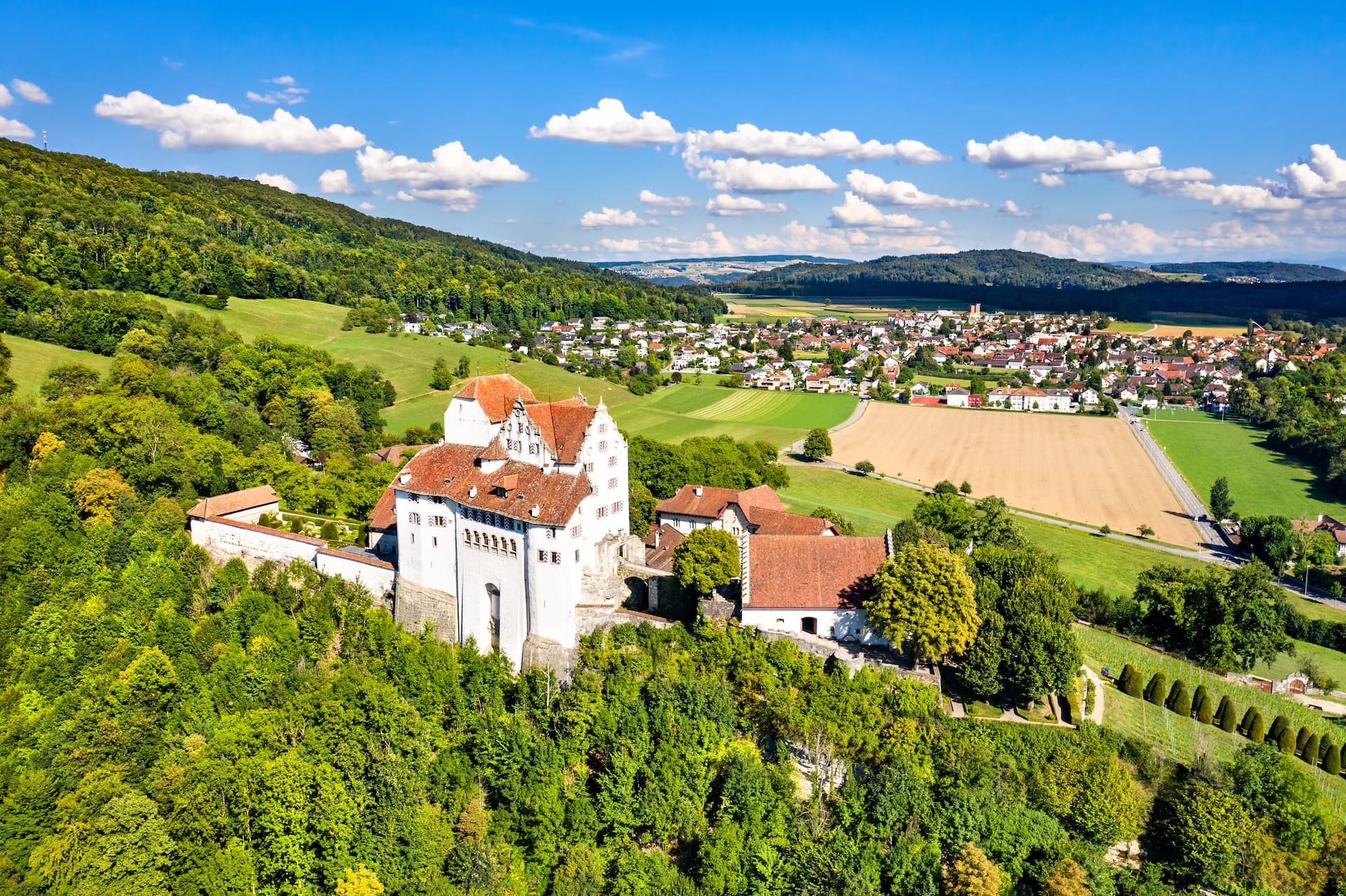 Aerial view of Wildegg Castle in Aargau, Switzerland, above green hills and a town.