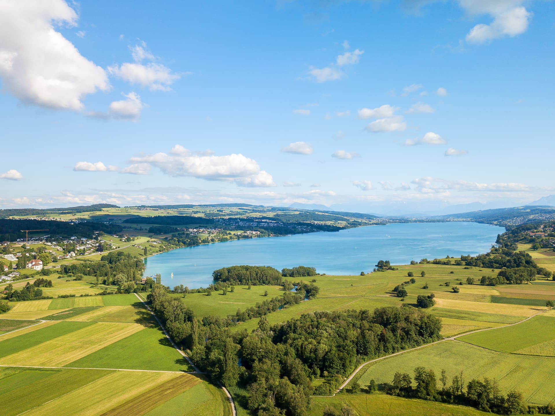 Aerial view of turquoise Lake Hallwil with green fields and Seengen, Switzerland in the distance.