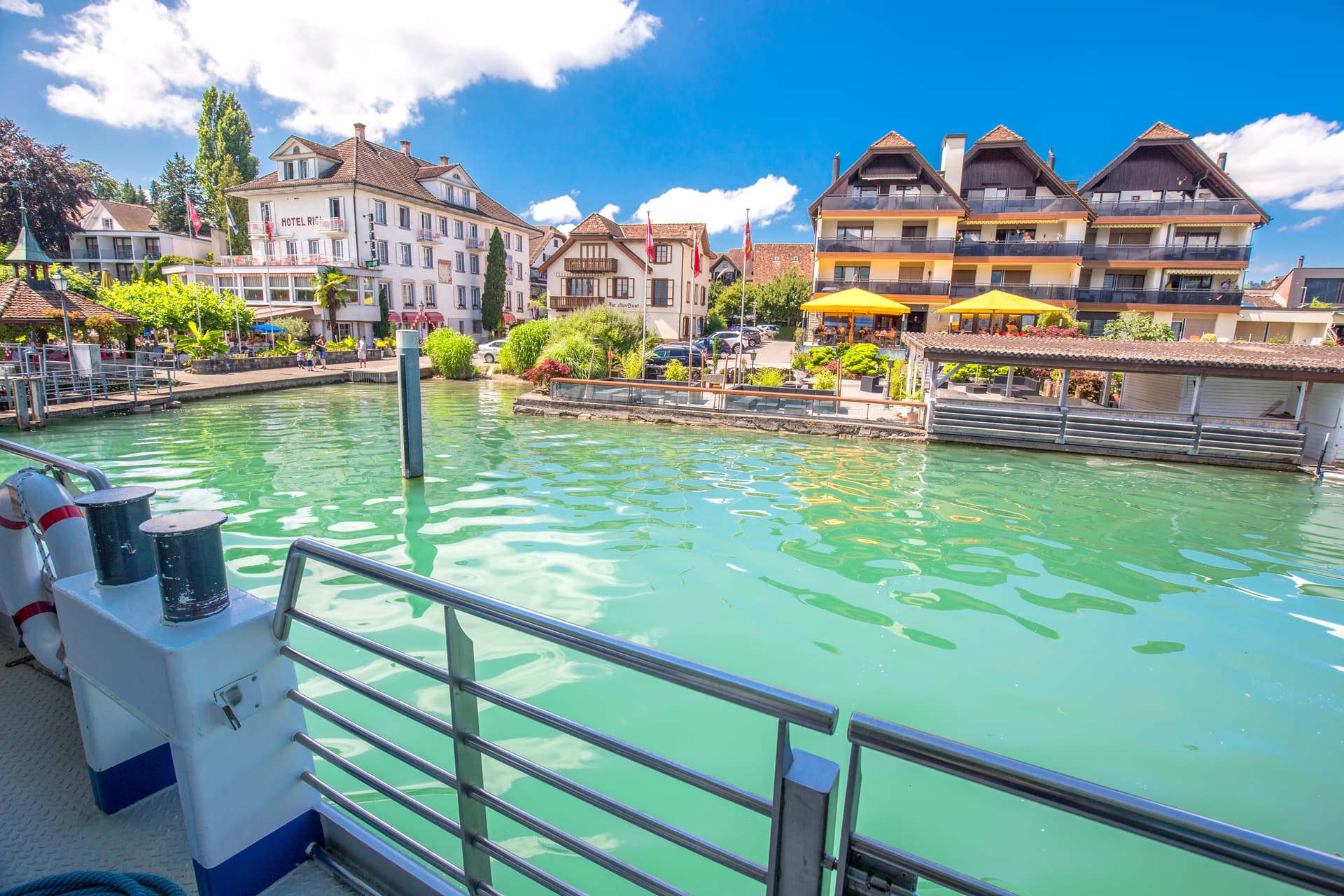Boat railing view of Immensee village on Lake Zug shoreline on a sunny day, Switzerland.