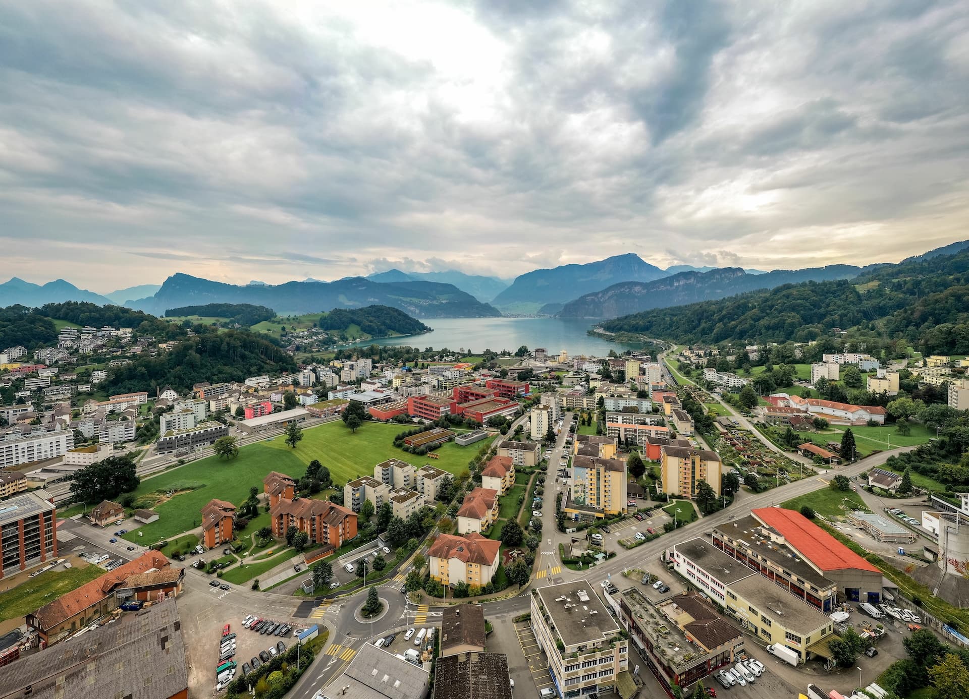 Aerial view of Lucerne-Horw town buildings, Lake Lucerne, and surrounding mountains under cloudy sky.