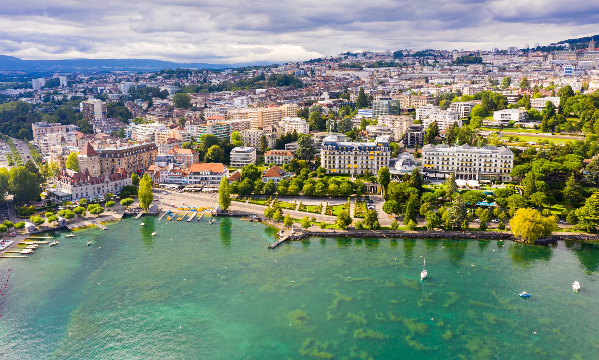 View from Lake Leman of Lausanne residential areas, green trees, and cloudy summer sky in Vaud.
